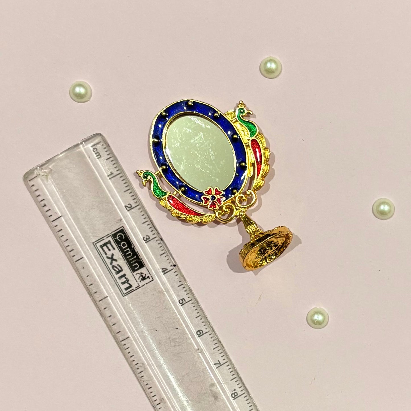 Close-up of the miniature metal Darpan with intricate gold-tone detailing, a decorative mirror for deity shringar and daily worship